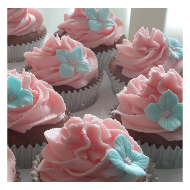 Zart rosa-farbende Cupcake-Creme mit je einer hellblauen Hortensienblüte
